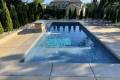 inground backyard pool surrounded by deck and manicured landscaping