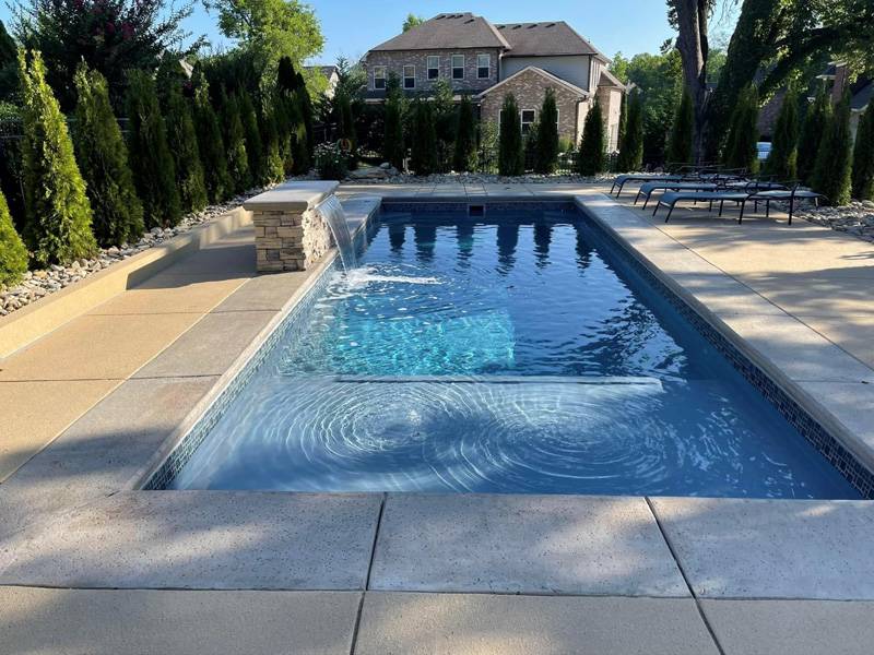 inground backyard pool surrounded by deck and manicured landscaping